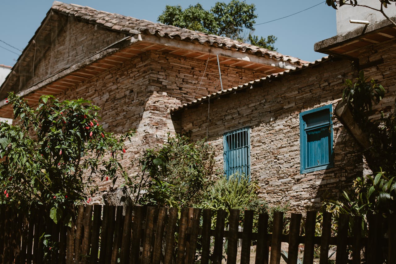 Charming rustic stone house with vibrant blue windows and lush garden foliage.