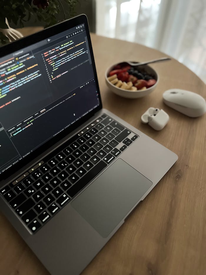 Cozy workspace featuring a laptop, mouse, and healthy fruit bowl on a wooden table.